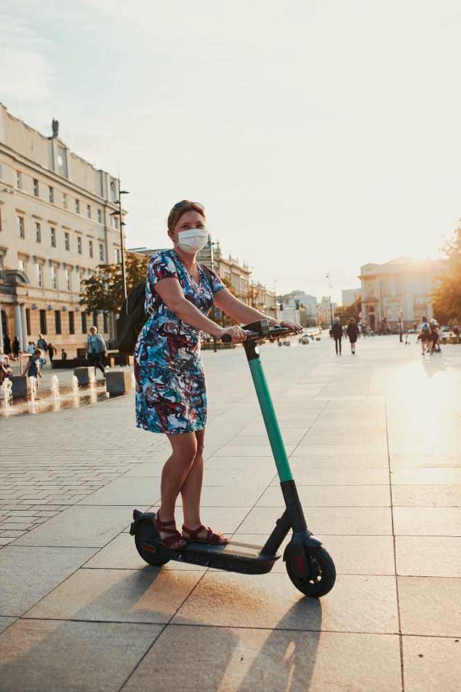 Young woman riding an electric scooter in the city center. Woman wearing the face mask to avoid virus infection and to prevent the spread of disease in time of coronavirus. Candid people, real moments, authentic situations