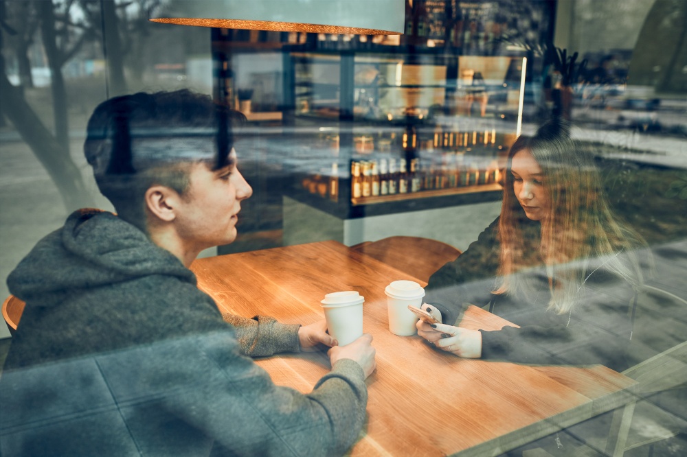 Friends having a chat, talking together, drinking coffee, sitting in a cafe. Young man and woman relaxing in cafe, having a break