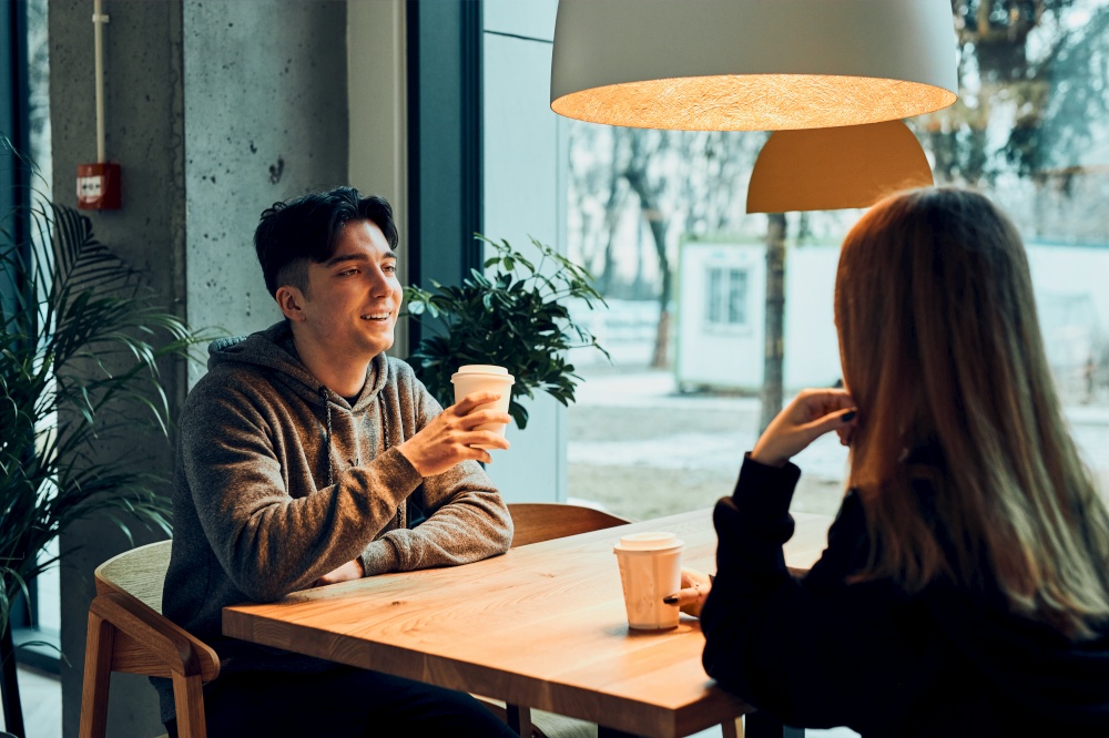 Friends having a chat, talking together, drinking coffee, sitting in a cafe. Young man and woman having a break, relaxing in cafe