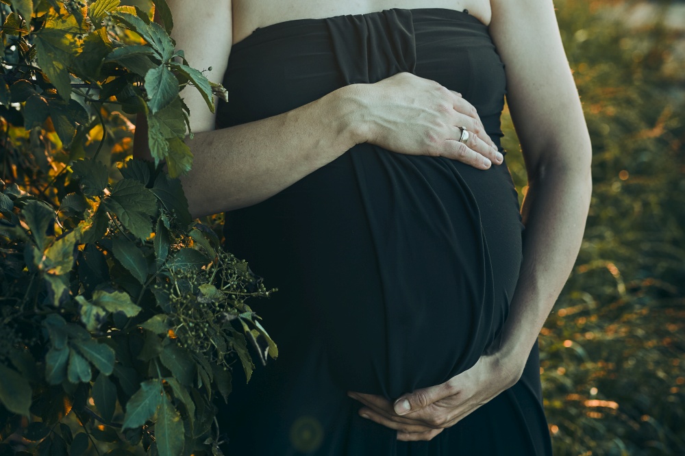 Pregnant woman hugging her tummy standing outdoors surrounded by nature. Pregnancy, expectation, motherhood concept