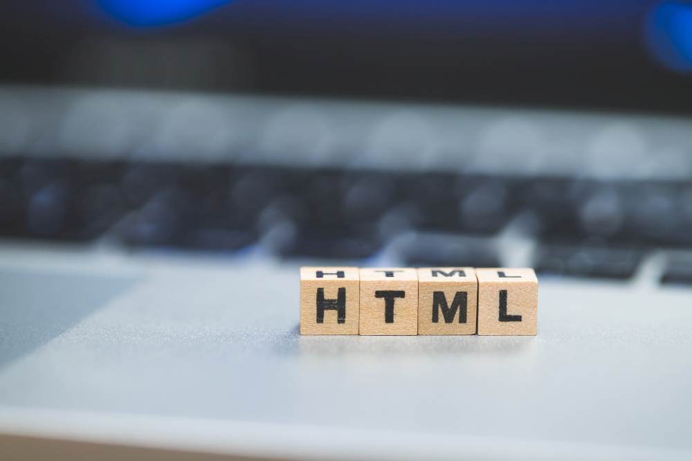 Wooden cubes with the letters “HTML” are lying on a laptop