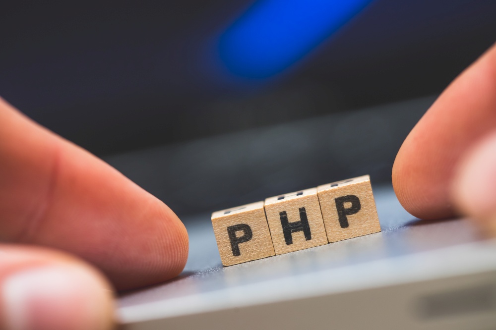 Wooden cubes with the letters “PHP” are lying on a laptop