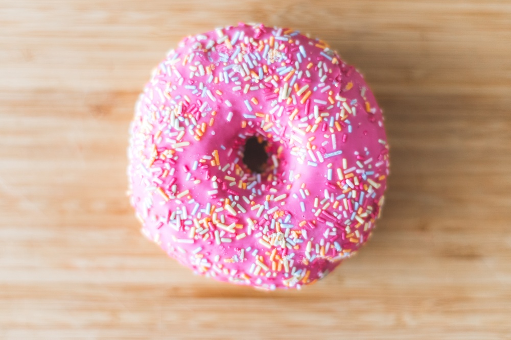 Sugar sprinkled pink donut on wooden plate