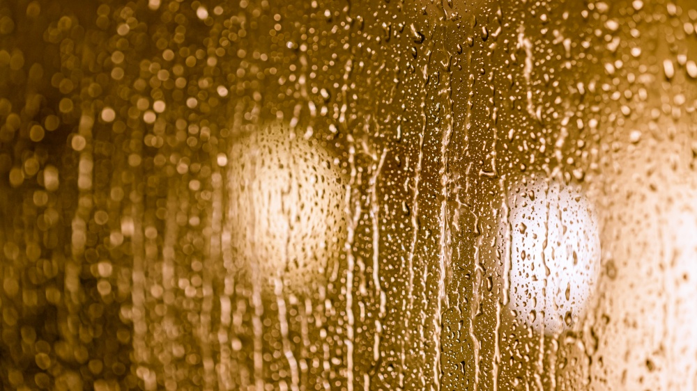 Close up of rain drops on the window in rainy night, warm lights