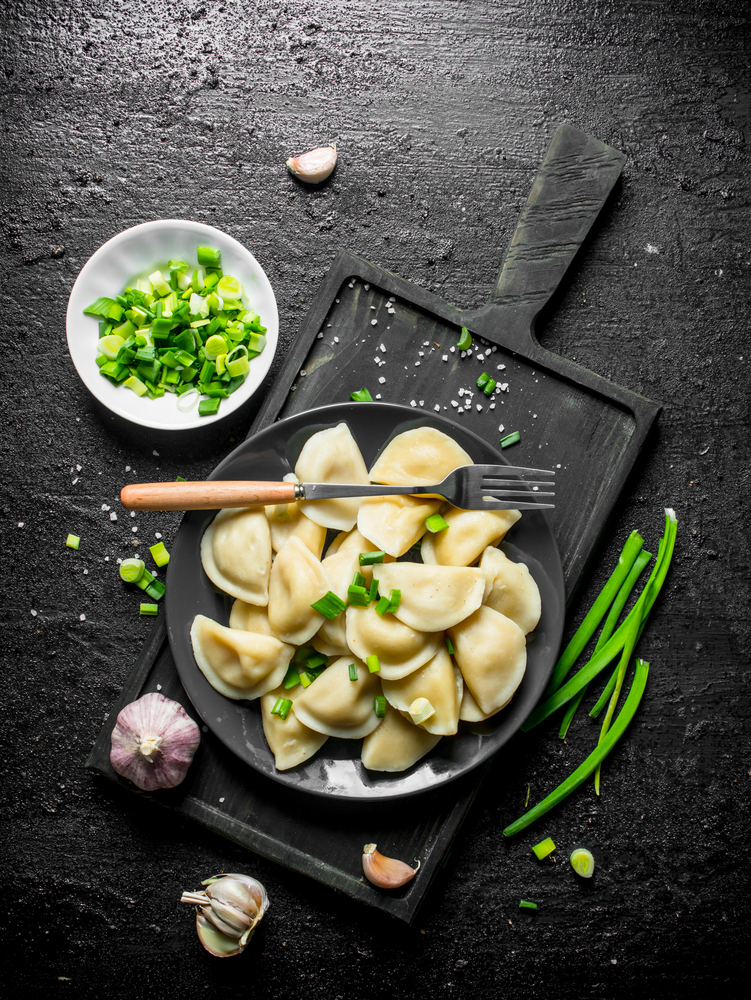 Dumplings on a plate with green onions and garlic. On black rustic background. Dumplings on a plate with green onions and garlic.