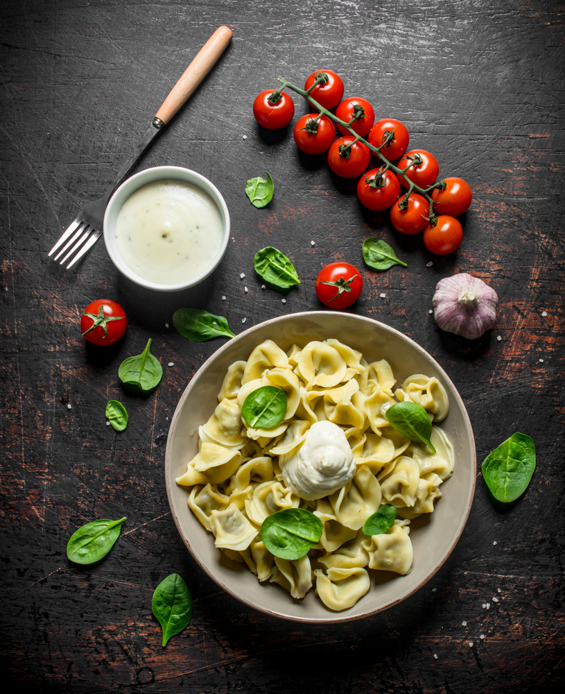 Dumplings with spinach, sour cream and tomatoes. On dark rustic background. Dumplings with spinach, sour cream and tomatoes.