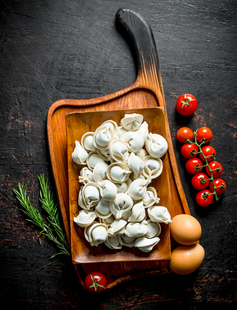 Raw dumpling with tomatoes and rosemary. On dark rustic background. Raw dumpling with tomatoes and rosemary.