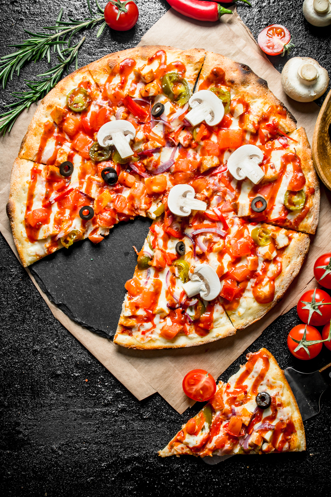 Fragrant sliced Mexican pizza with mushrooms and tomatoes. On black rustic background. Fragrant sliced Mexican pizza with mushrooms and tomatoes.