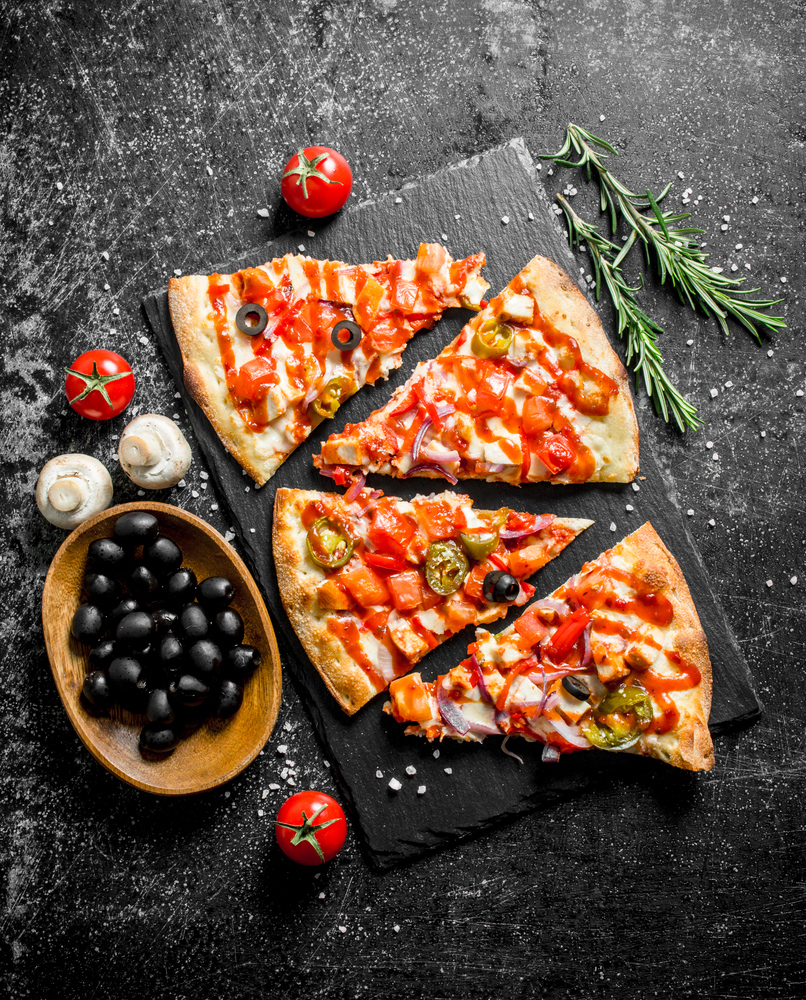 Slices of Mexican pizza with tomatoes, olives and rosemary. On dark rustic background. Slices of Mexican pizza with tomatoes, olives and rosemary.