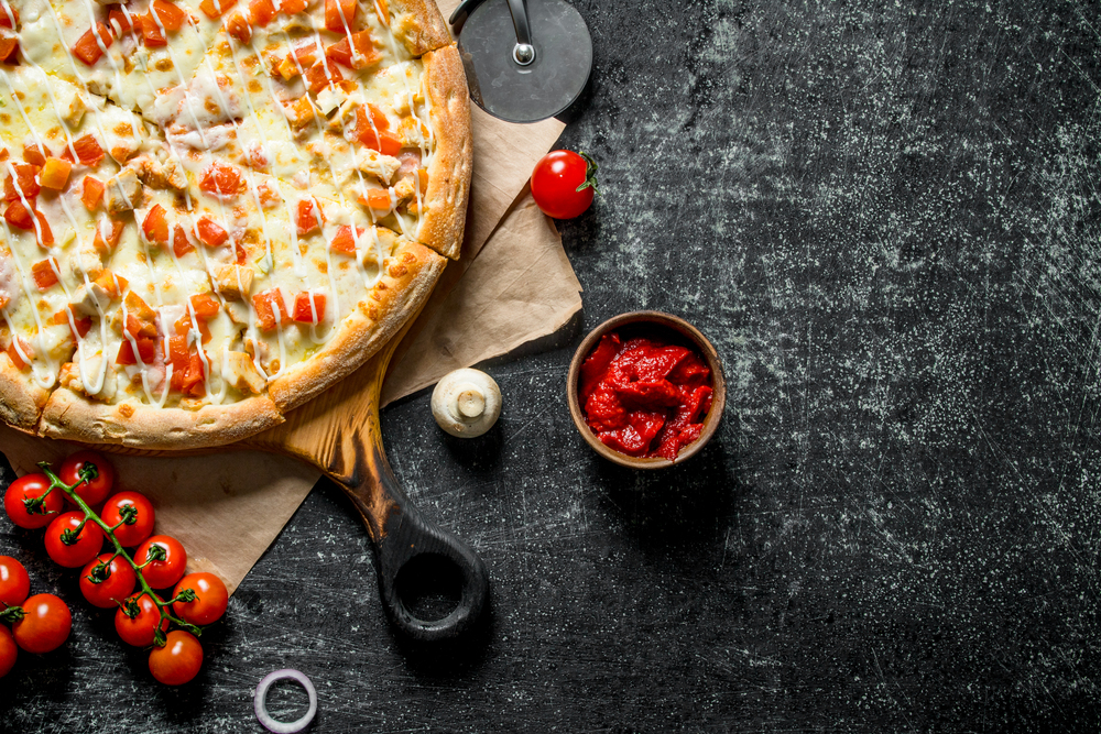 Hot pizza on paper with cherry tomatoes. On dark rustic background. Hot pizza on paper with cherry tomatoes.