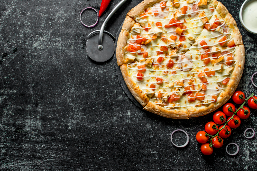 Sliced pizza with cherry tomatoes, onion rings and cheese sauce in bowl. On dark rustic background. Sliced pizza with cherry tomatoes, onion rings and cheese sauce in bowl.