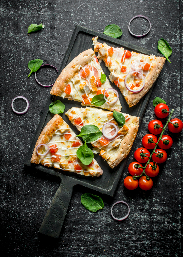 Slices of pizza with tomatoes on a branch and spinach. On dark rustic background. Slices of pizza with tomatoes on a branch and spinach.