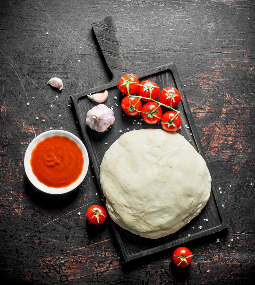 Dough with cherry tomatoes and garlic. On dark rustic background. Dough with cherry tomatoes and garlic.