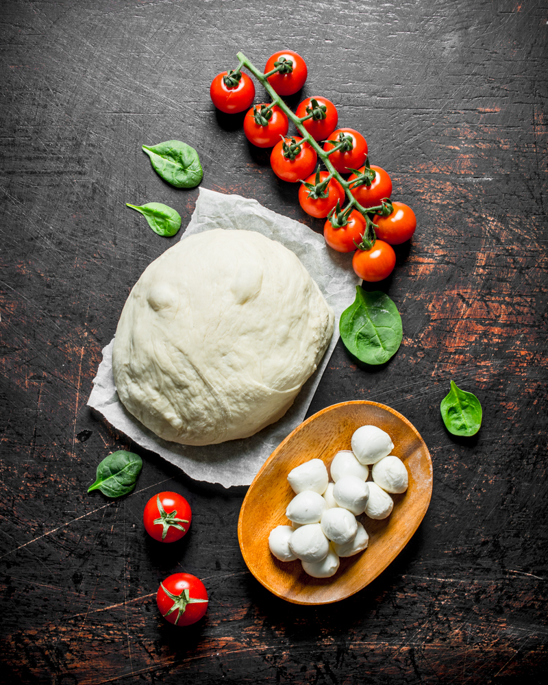 Pizza dough with mozzarella and cherry tomatoes. On dark rustic background. Pizza dough with mozzarella and cherry tomatoes.