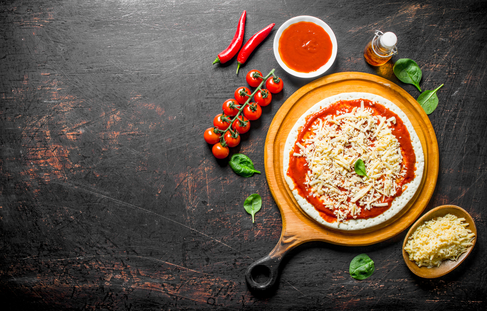 Preparation pizza. Rolled out dough with tomato paste, cheese and cherry tomatoes. On dark rustic background. Preparation pizza. Rolled out dough with tomato paste, cheese and cherry tomatoes.