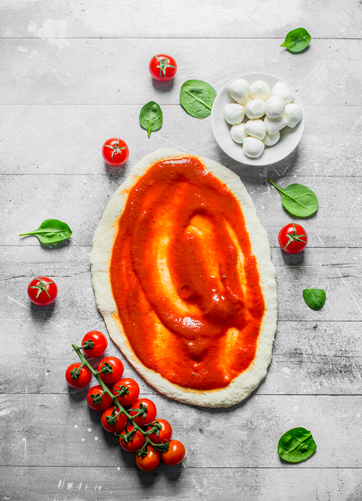 Preparation pizza. Rolled out dough with tomato paste, mozzarella and spinach. On white wooden background. Preparation pizza. Rolled out dough with tomato paste, mozzarella and spinach.