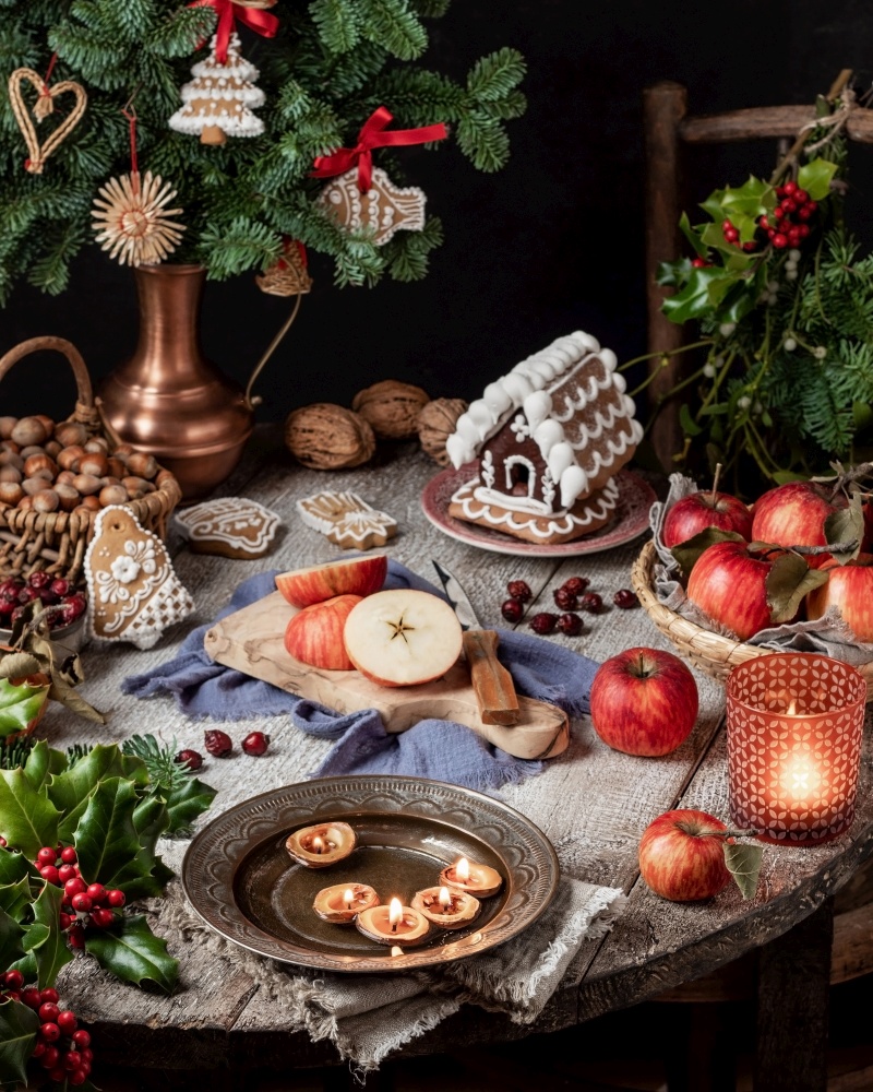 Christmas still life with candles made from nut shells floating in a bowl of water, gingerbread cookies and apples
