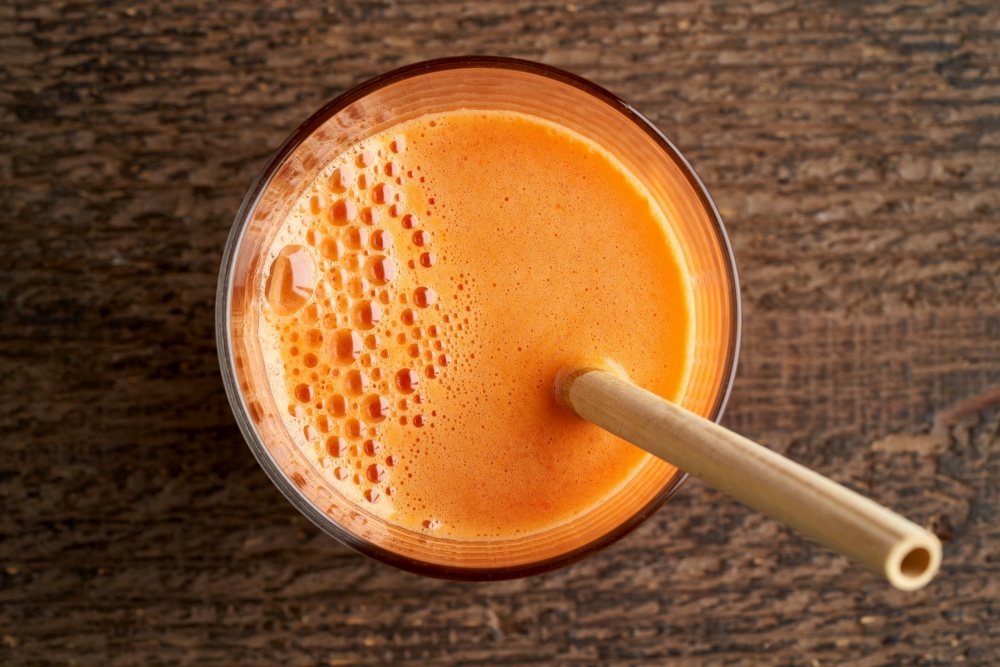 A glass of carrot juice with a bamboo straw, top view