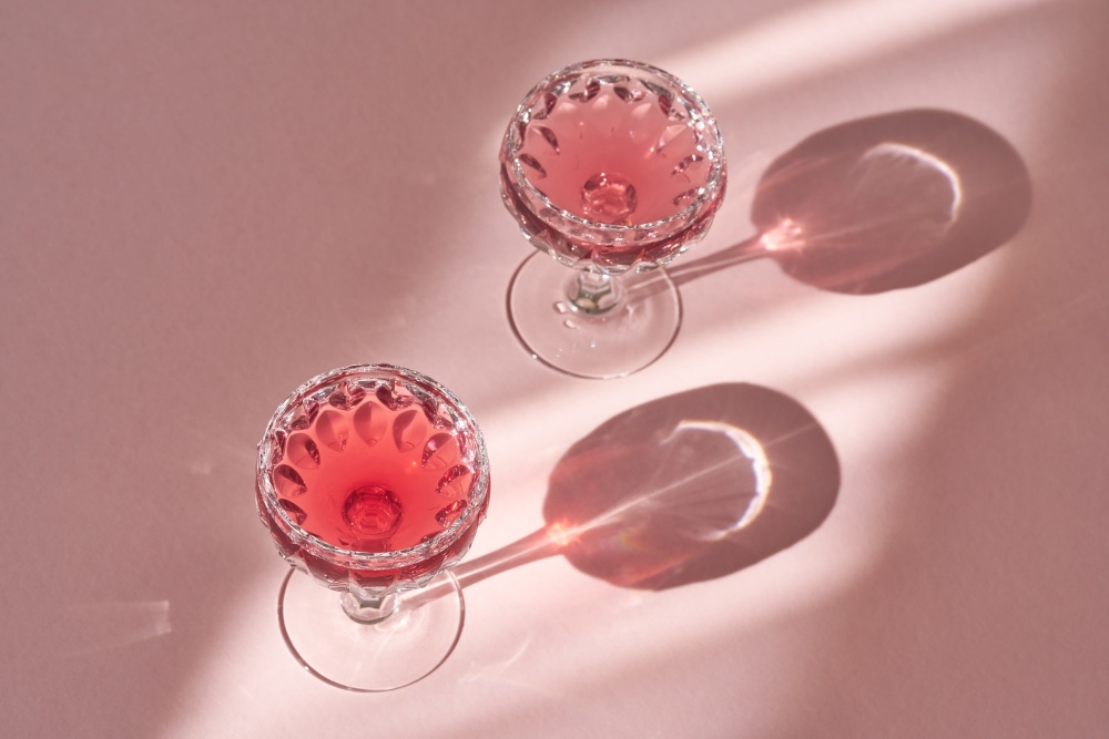 Water with black elder syrup in two glasses on pink background