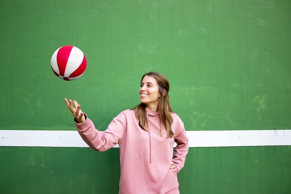 Teenager female playing basketball over green wall