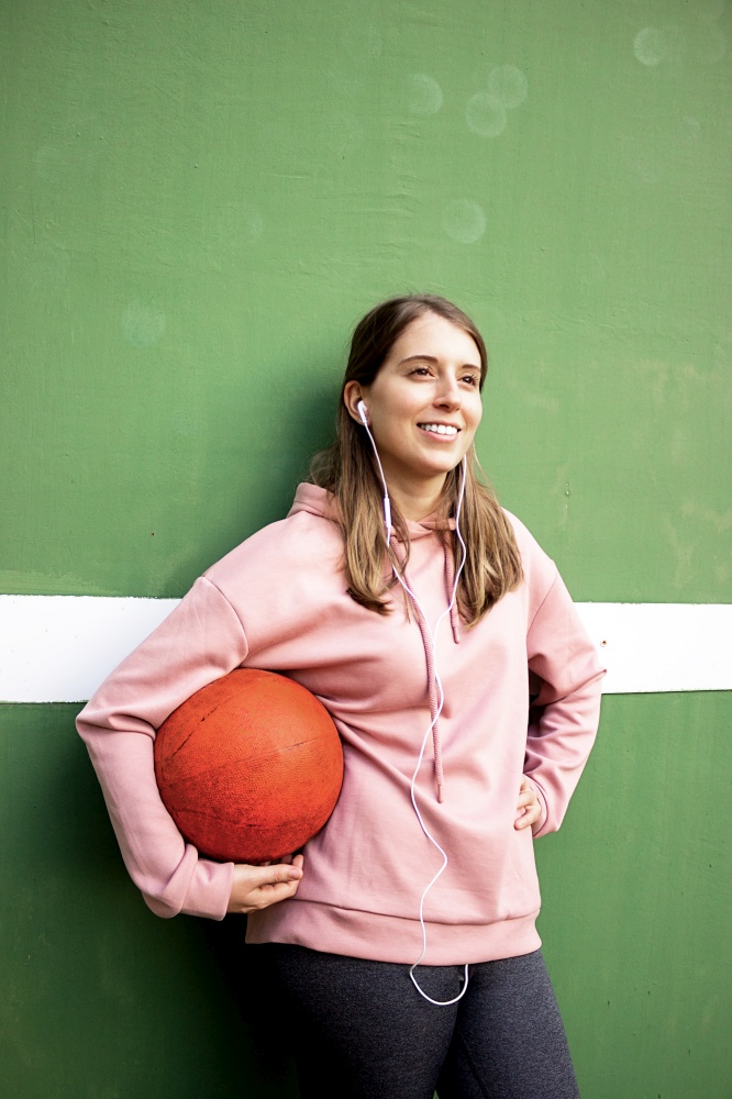 young long haired girl holding a basket ball against green wall