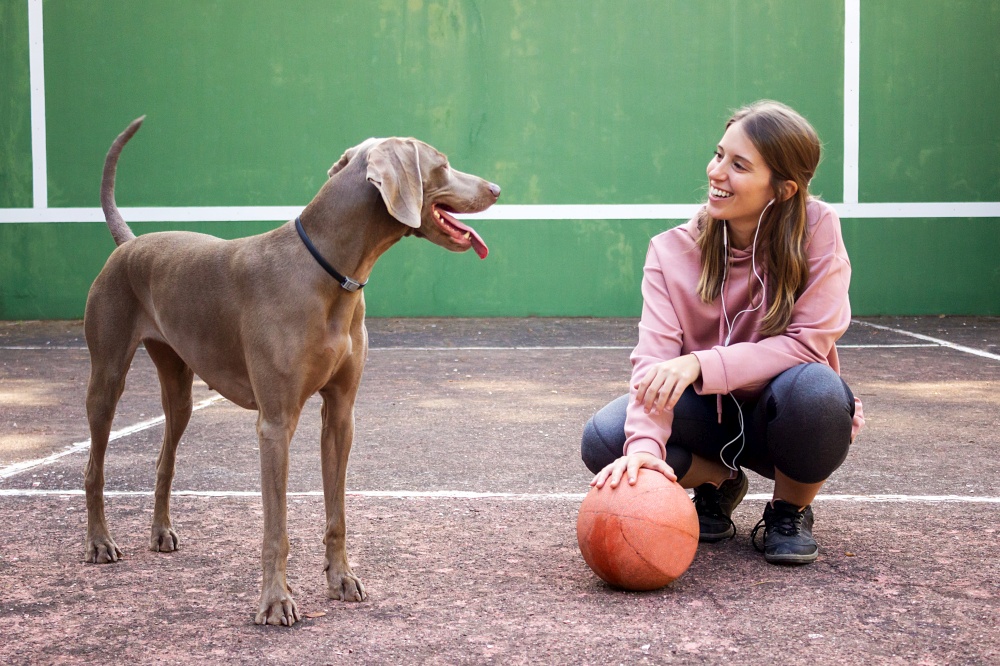 Young female holding ball posing with her dog