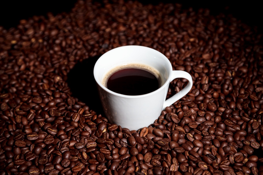 A wihte cup with some coffee beans on a black background