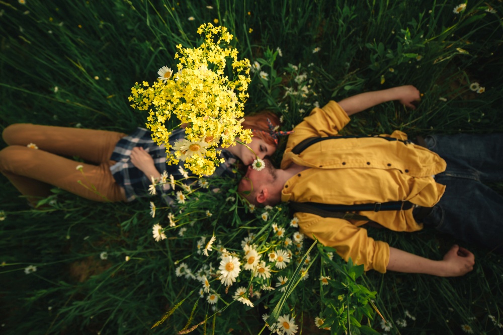 Playful happy handsome couple having while walking in woods. tourists in the mountains. Adventure in nature concept. happy young couple man and redhead woman lying on bright green grass on summer day, top view. Love story.