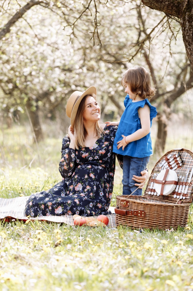 beautiful pregnant woman with little daughter playing on a picnic in a blooming spring garden.. beautiful pregnant woman with little daughter playing on a picnic in a blooming spring garden