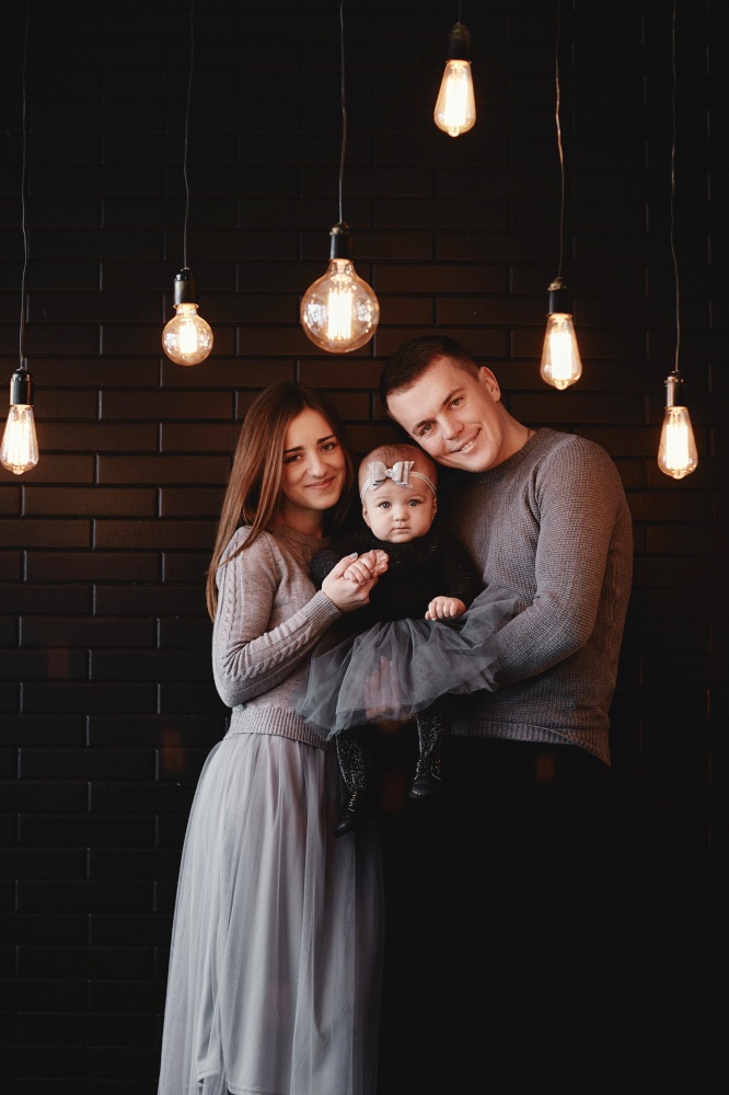 portrait of young family dad, mom and baby girl enjoy time together at home. Retro light bulbs in the foreground. Christmas time. portrait of young family dad, mom and baby girl enjoy time together at home. Retro light bulbs in the foreground. Christmas time.