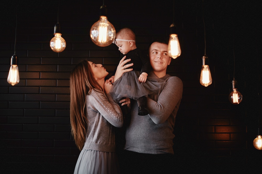 portrait of young family dad, mom and baby girl enjoy time together at home. Retro light bulbs in the foreground. Christmas time. portrait of young family dad, mom and baby girl enjoy time together at home. Retro light bulbs in the foreground. Christmas time.