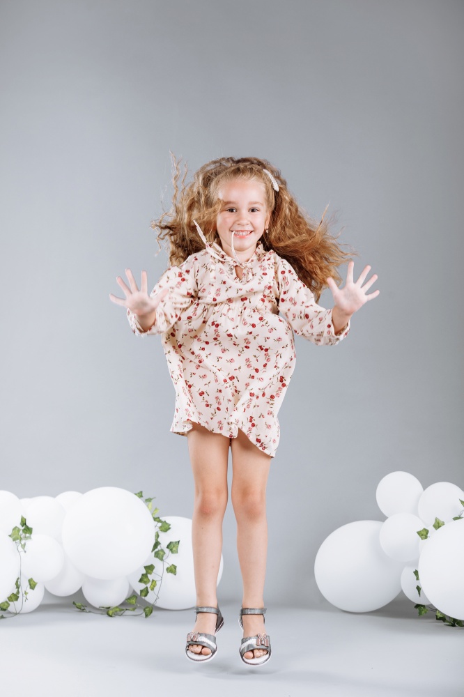 Cute little girl blonde smiling having fun. child in floral dress jumping with white balloons and greens and celebration easter. happy childhood.. Cute little girl blonde smiling having fun. child in floral dress jumping with white balloons and greens and celebration easter. happy childhood