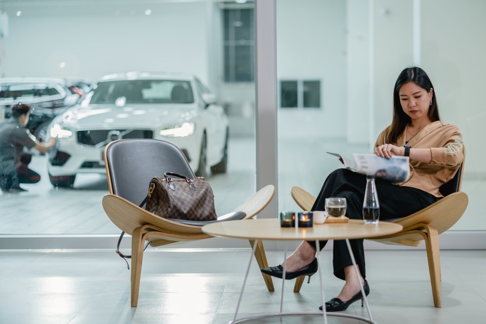 Asian customer woman reading and waiting mechanic checking for maintain her car in maintainance service center with the part of showroom