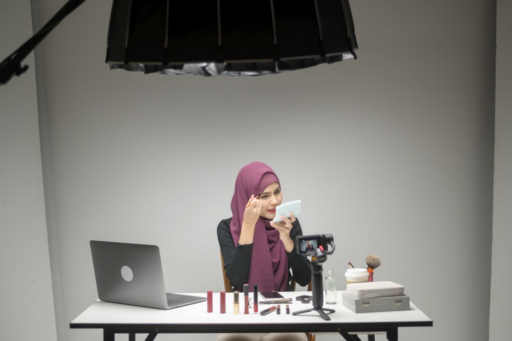 A young muslim woman entrepreneur working with laptop presents cosmetic products during online live stream over white background studio, selling online and beauty blogger concept. young muslim woman entrepreneur working with laptop presents cosmetic products during online live stream over white background studio, selling online and beauty blogger concept