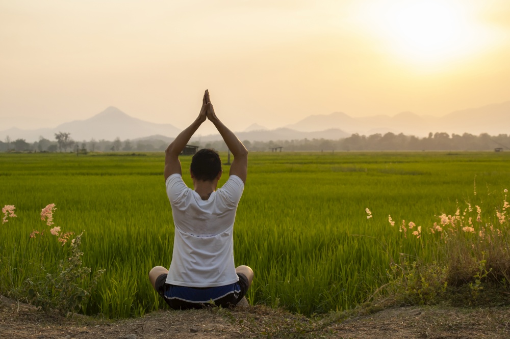young man practicing yoga on the rice field at sunset. Meditation