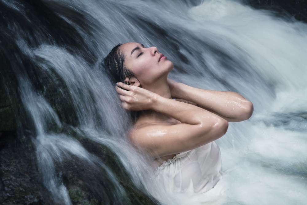 Beautiful woman model closed her eye posing under waterfall wearing white swimwear