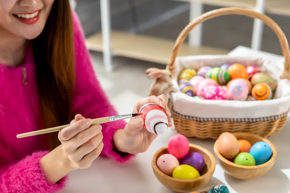 Easter holiday concept, Happy Asian Young woman wearing bunny ears hand painted eggs for Easter with colorful Easter eggs In the white room background