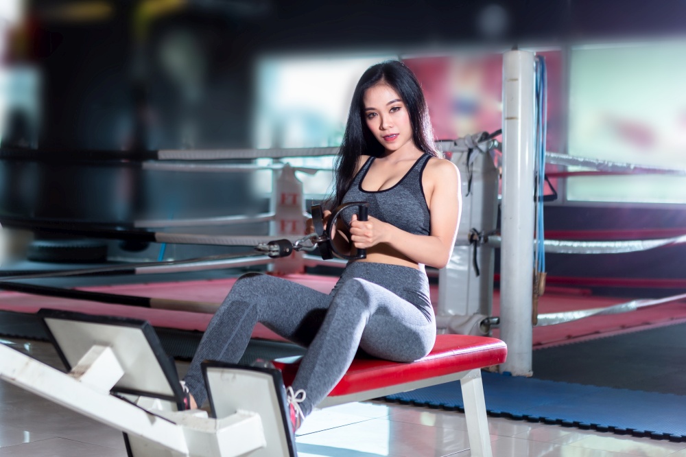 Fitness Asian women performing doing exercises training with rowing machine (Seat Cable Rows Machine) in sport gym interior and fitness health club with sports exercise equipment Gym.