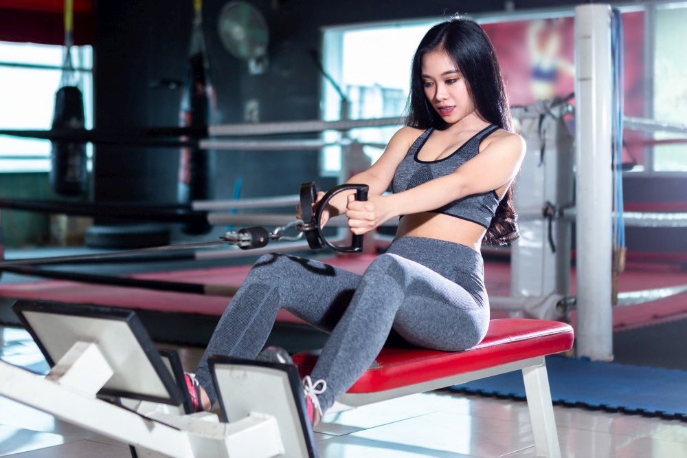 Fitness Asian women performing doing exercises training with rowing machine (Seat Cable Rows Machine) in sport gym interior and fitness health club with sports exercise equipment Gym.