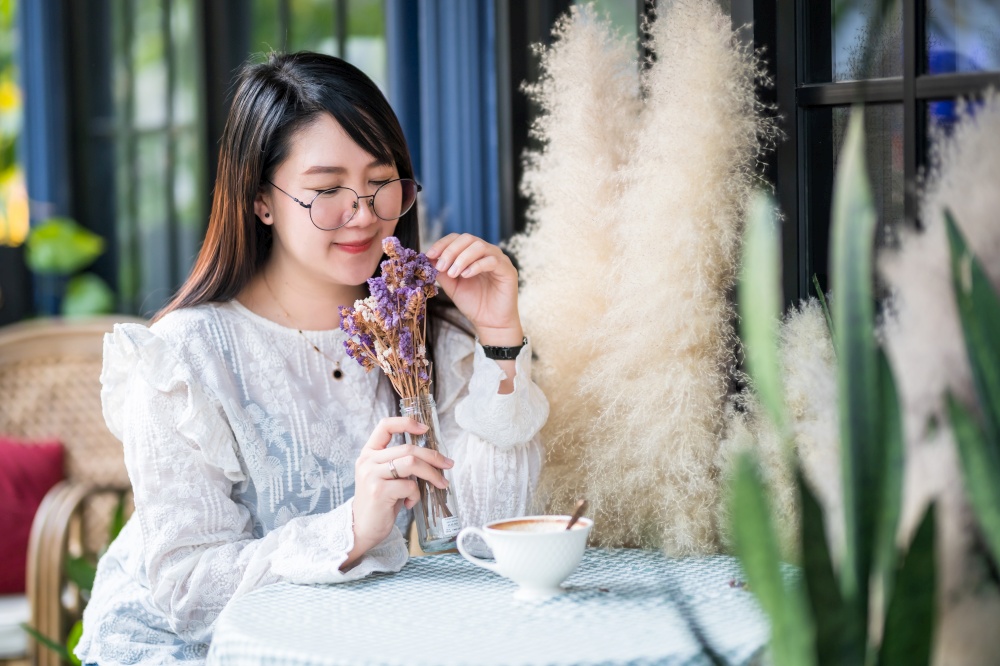 Portrait of Happy Attractive asian people cute woman smelling a purple flowers Bouquet of lavender with coffee cup felt like relaxing in coffee shop like the background