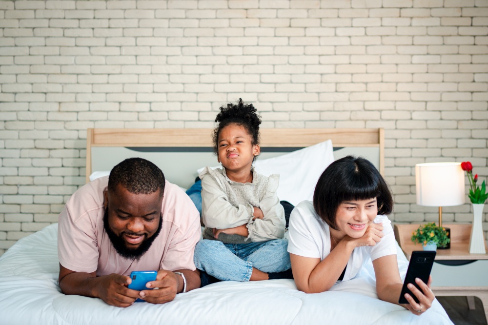 African American girls are not satisfied and sad, sitting in the middle between father and mother. Parents Are using the smartphone and abandoned children. Children need their parents attention.