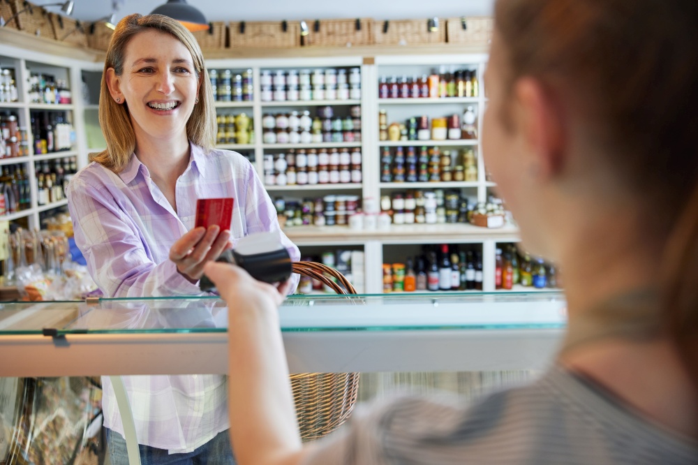 Smiling Female Customer Delicatessen Food Store Making Contactless Payment With Card For Shopping To Sales Assistant