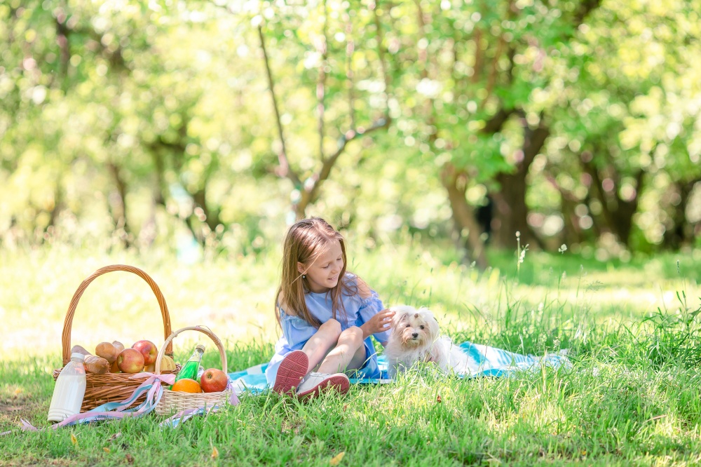 Happy kid on picnic plays with white puppy on green grass in spring cherry garden. Little kid with puppy on picnic in the park