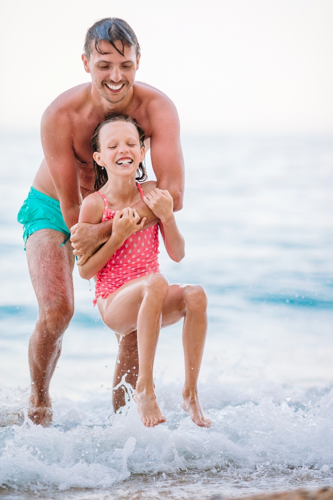 Young father with his daughter have fun in shallow water on the beach. Summer family vacation. Father and his daughter enjoy beach vacation
