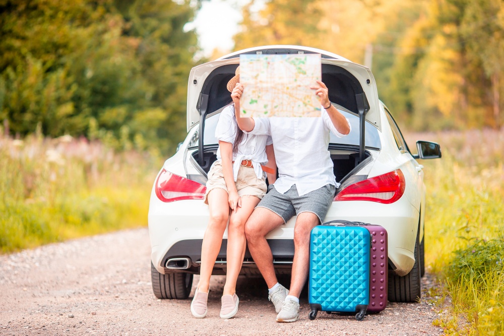 Young travelers looking at map while sitting in trunk of a car. Summer car vacation. Young couple tourist enjoying on summer vacation