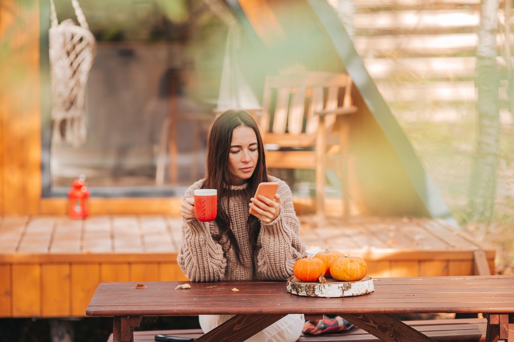 Young woman outdoors in autumn. Happy young woman drinking coffee sitting at the wooden table outdoors