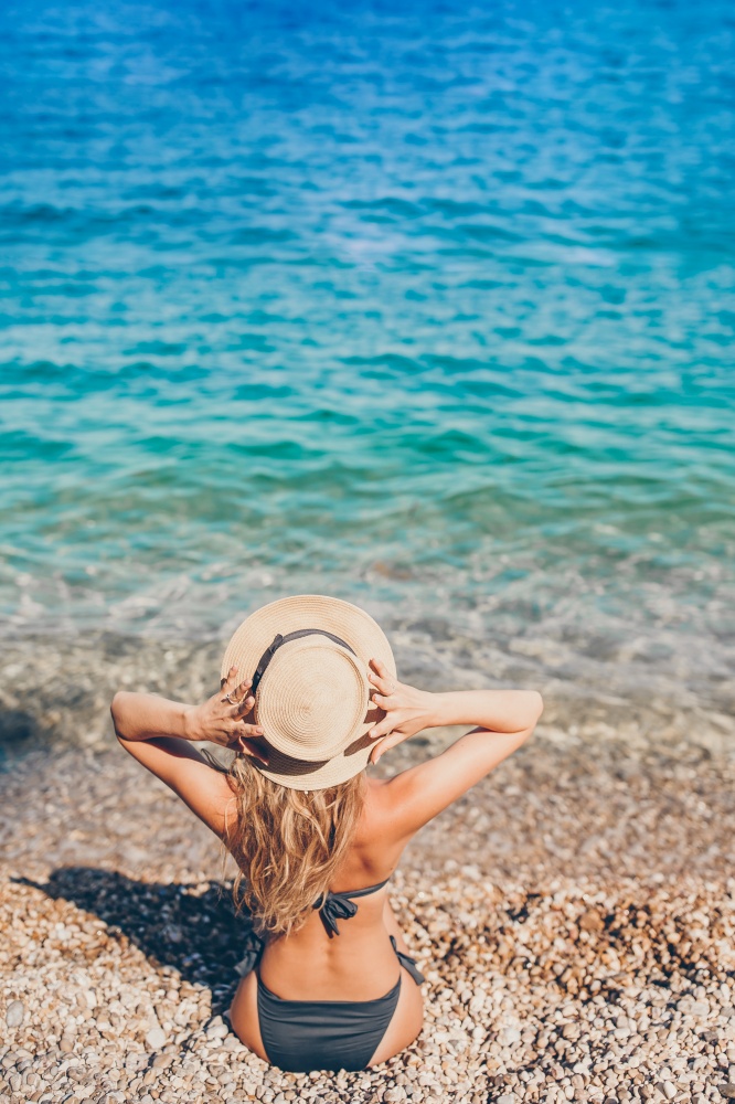 Woman laying on the beach in straw hat enjoying summer holidays looking at the sea. Young beautiful woman relaxing at european beach