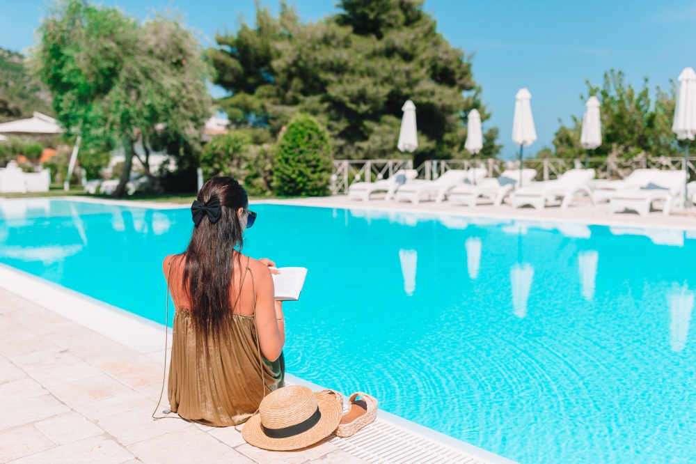 Woman reads book by the pool in a luxurious hotel resort enjoying perfect beach holiday vacation. Woman relaxing by the pool in a luxury hotel resort enjoying perfect beach holiday vacation