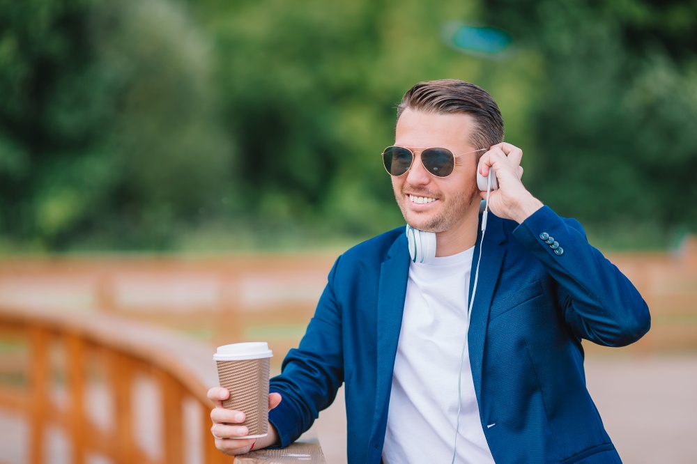 Young man with smartphone drinking coffee outdoors. Happy boy working by cellphone outdoor in the city. Happy young urban man working and drinking coffee in european city outdoors