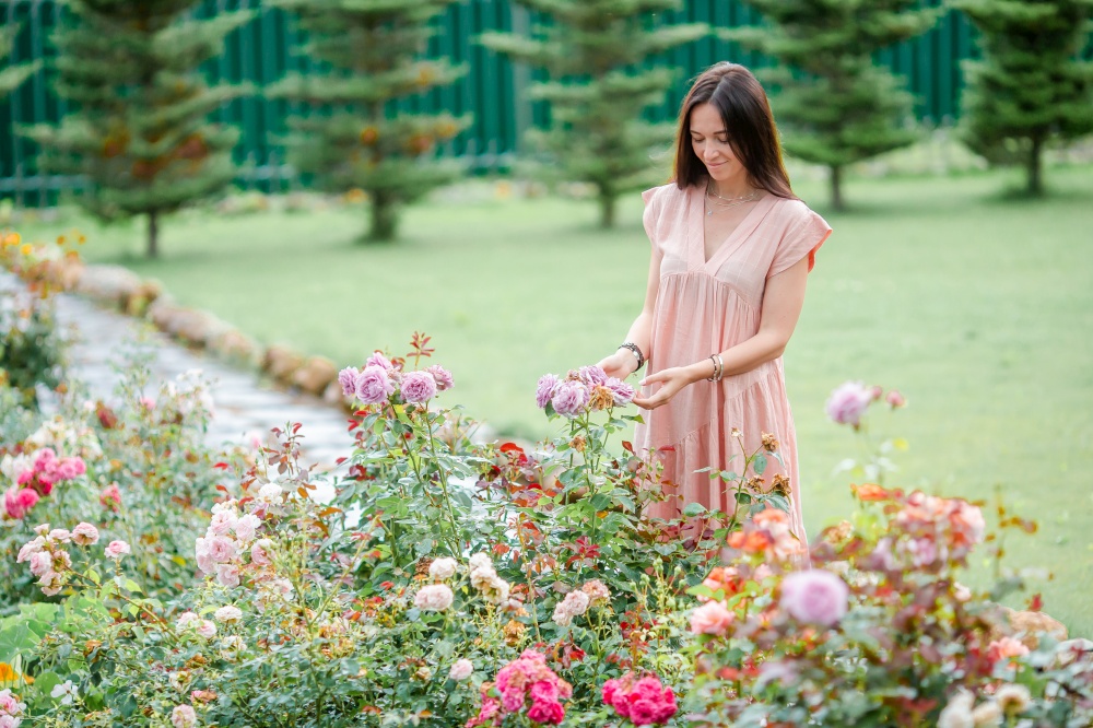Young woman in a flower garden among beautiful roses. Beautiful flavour of roses. Young girl in a flower garden among beautiful roses. Smell of roses
